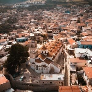Aerial view of a historic Greek town with a church and terracotta roofs.